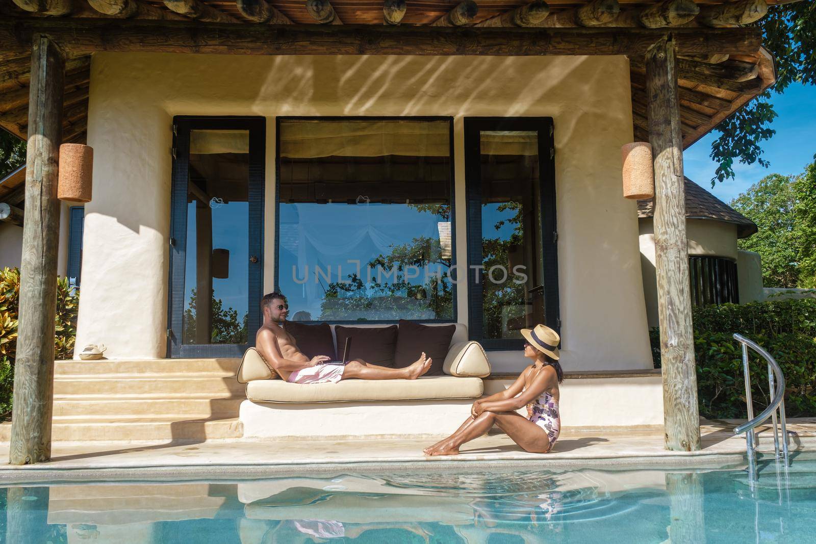 remote online working digital nomad men and women and laptop sitting pool at a private pool villa, by fokkebok