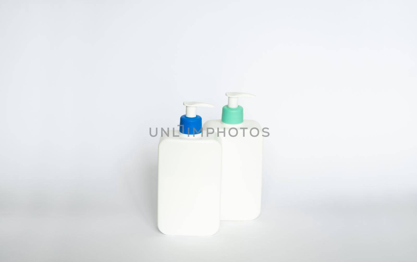 Two white cosmetic plastic bottle with pump dispenser pump and blue cap on white background. Liquid container for gel, lotion, cream, shampoo, bath foam. by vovsht