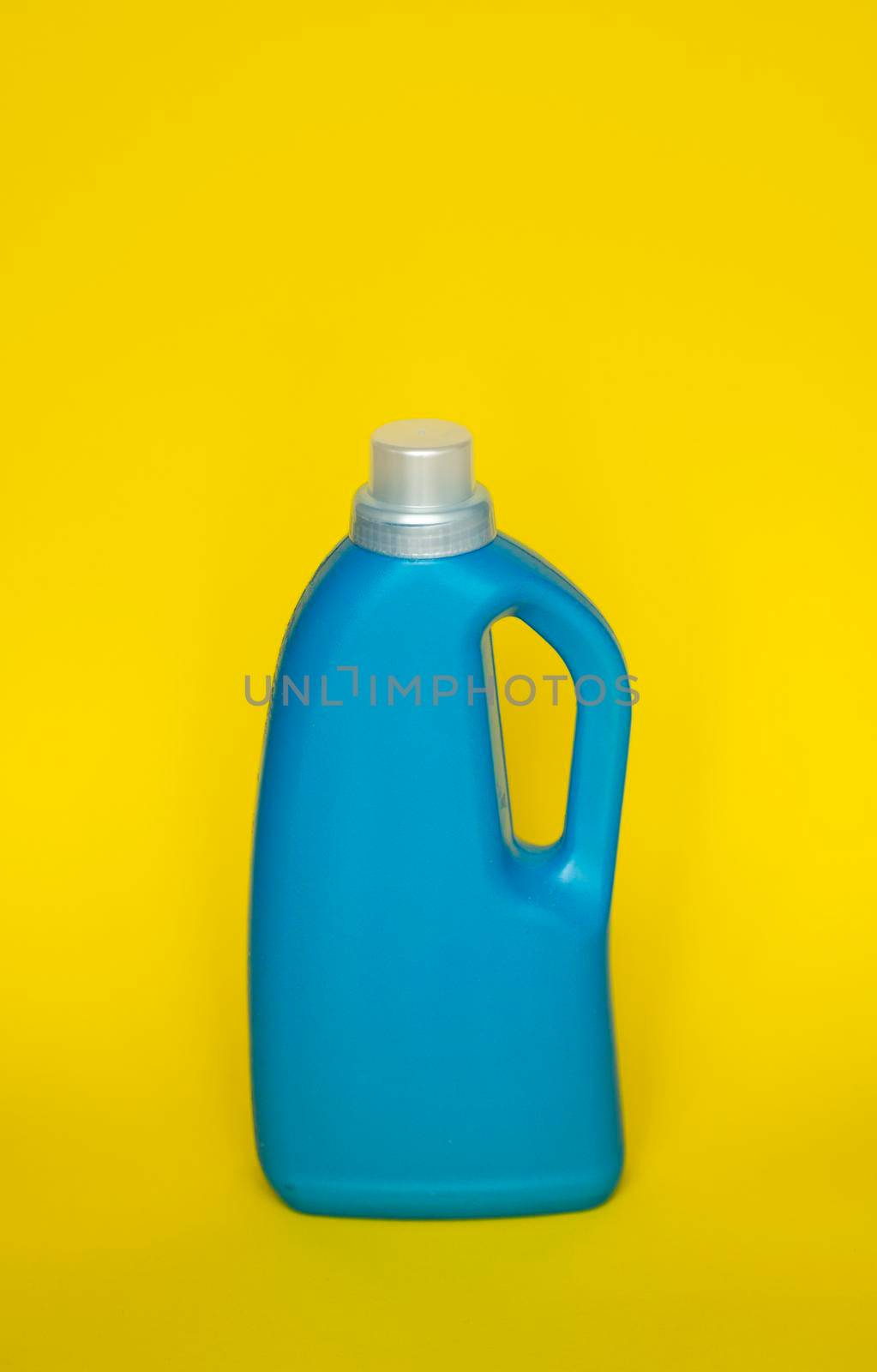 Blue plastic bottle stands on yellow background. Conditioner or liquid powder for washing. Capacity with space for copying. Layout for logo application. by vovsht