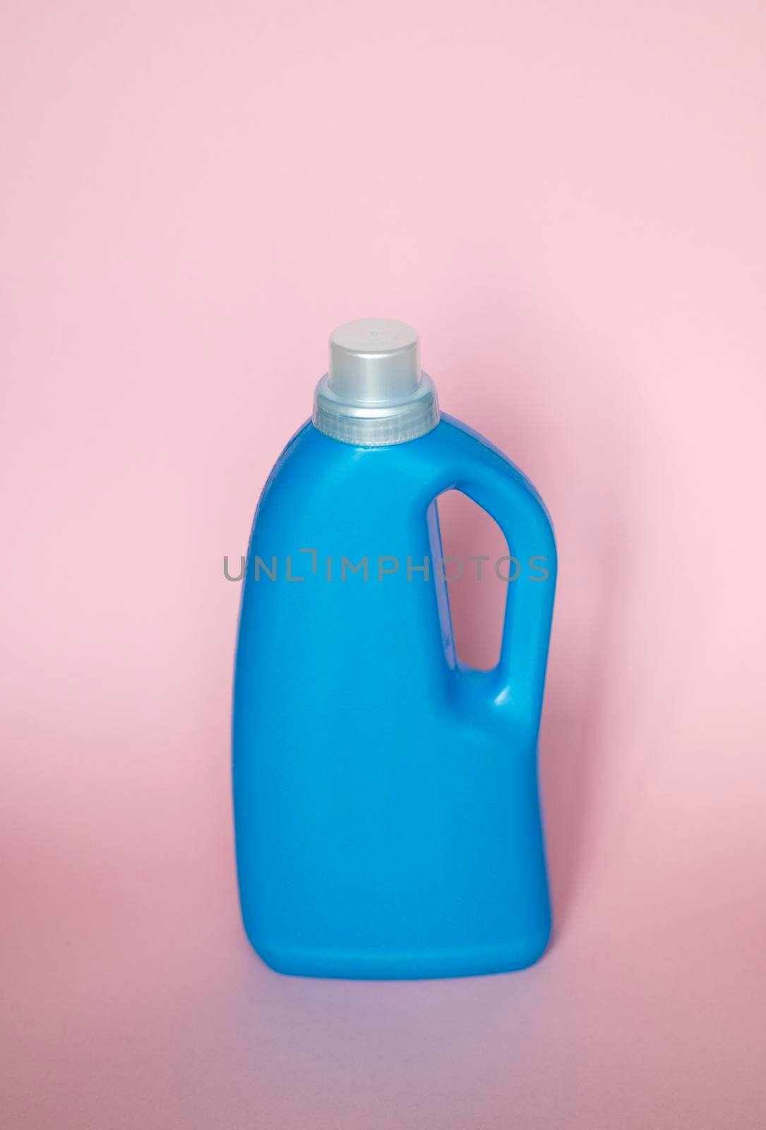 Blue plastic bottle stands on pink background. Conditioner or liquid powder for washing. Capacity with space for copying. Layout for logo application