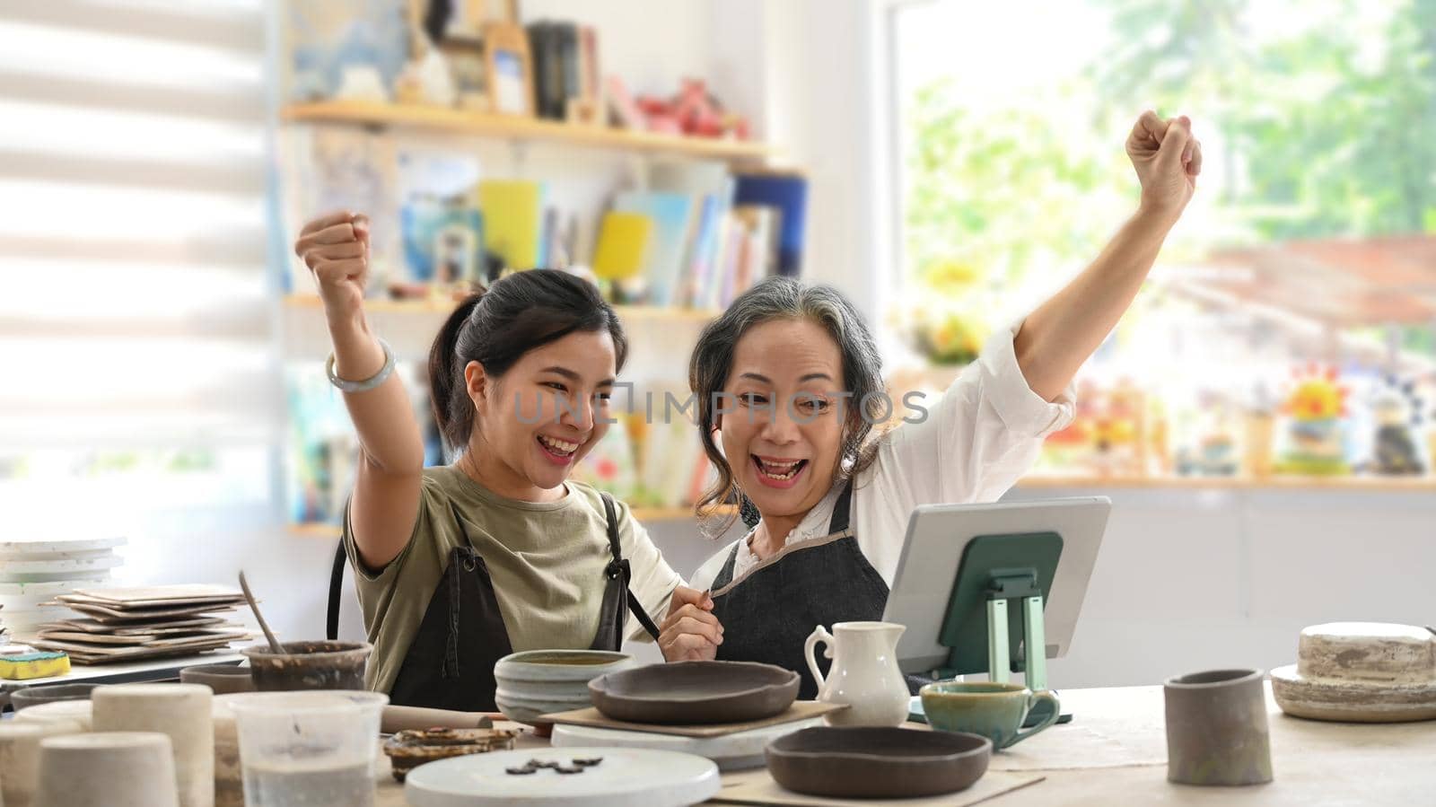 Happy craft pottery shop owners celebrating for sales success after checking order from online shopping on laptop. Online selling, E-commerce concept.