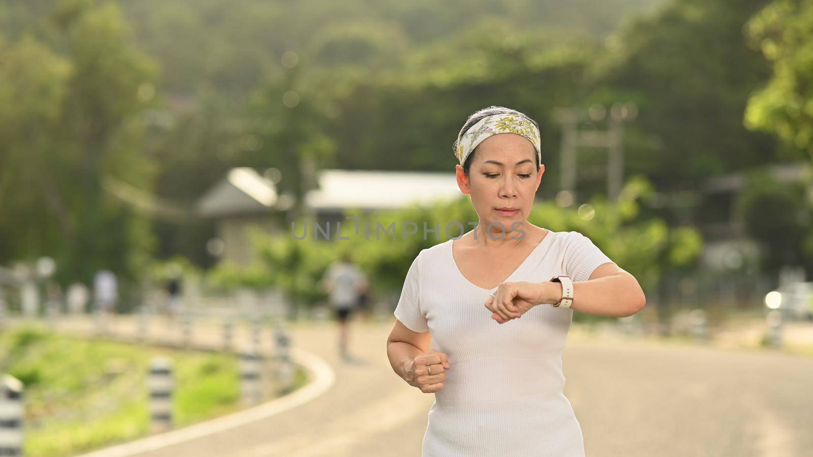 Sport middle aged woman checking fitness results or heart rate on smartwatch during workout. Healthy lifestyle, workout and wellness concept by prathanchorruangsak