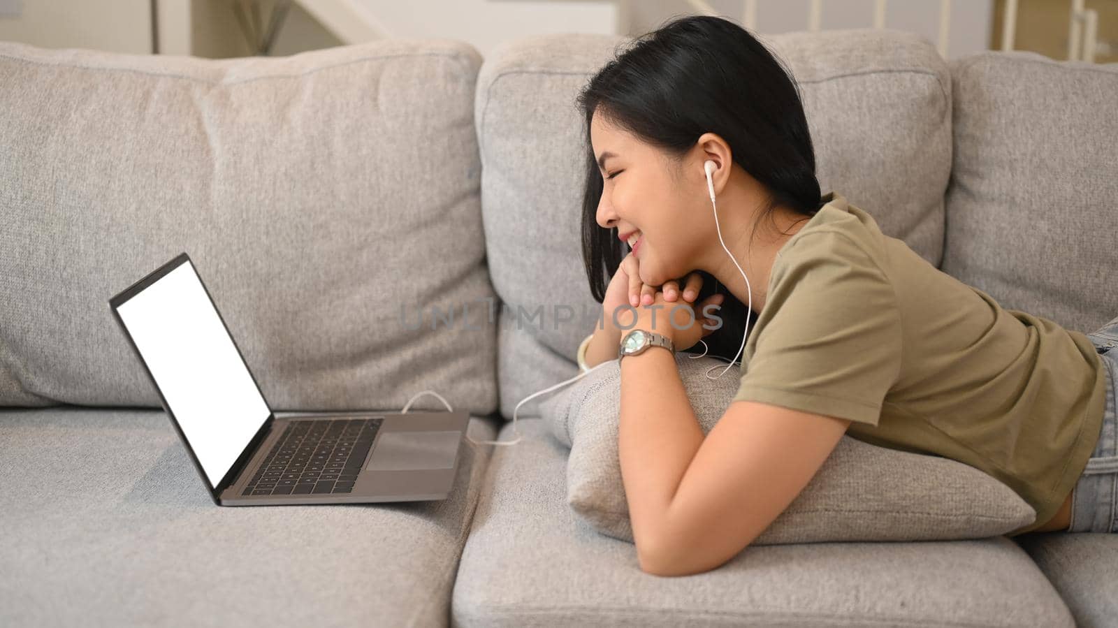 Smiling young woman relaxing in living room and talking by online virtual chat on computer laptop. Leisure activity and technology concept by prathanchorruangsak