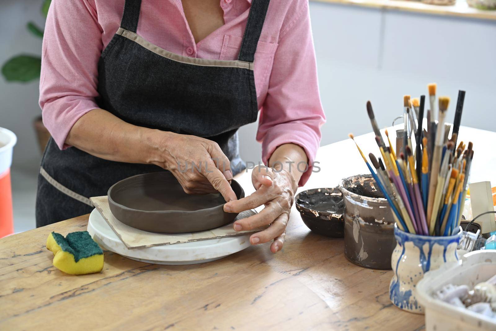 Cropped view of senior female creating handmade ceramic bowl in workshop. Indoors lifestyle activity, handicraft, hobbies concept.