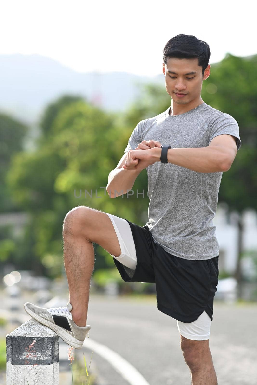 Athletic asian man checking his heart rate data on smartwatch during morning workout in the park. Healthy lifestyle, workout and wellness concept.