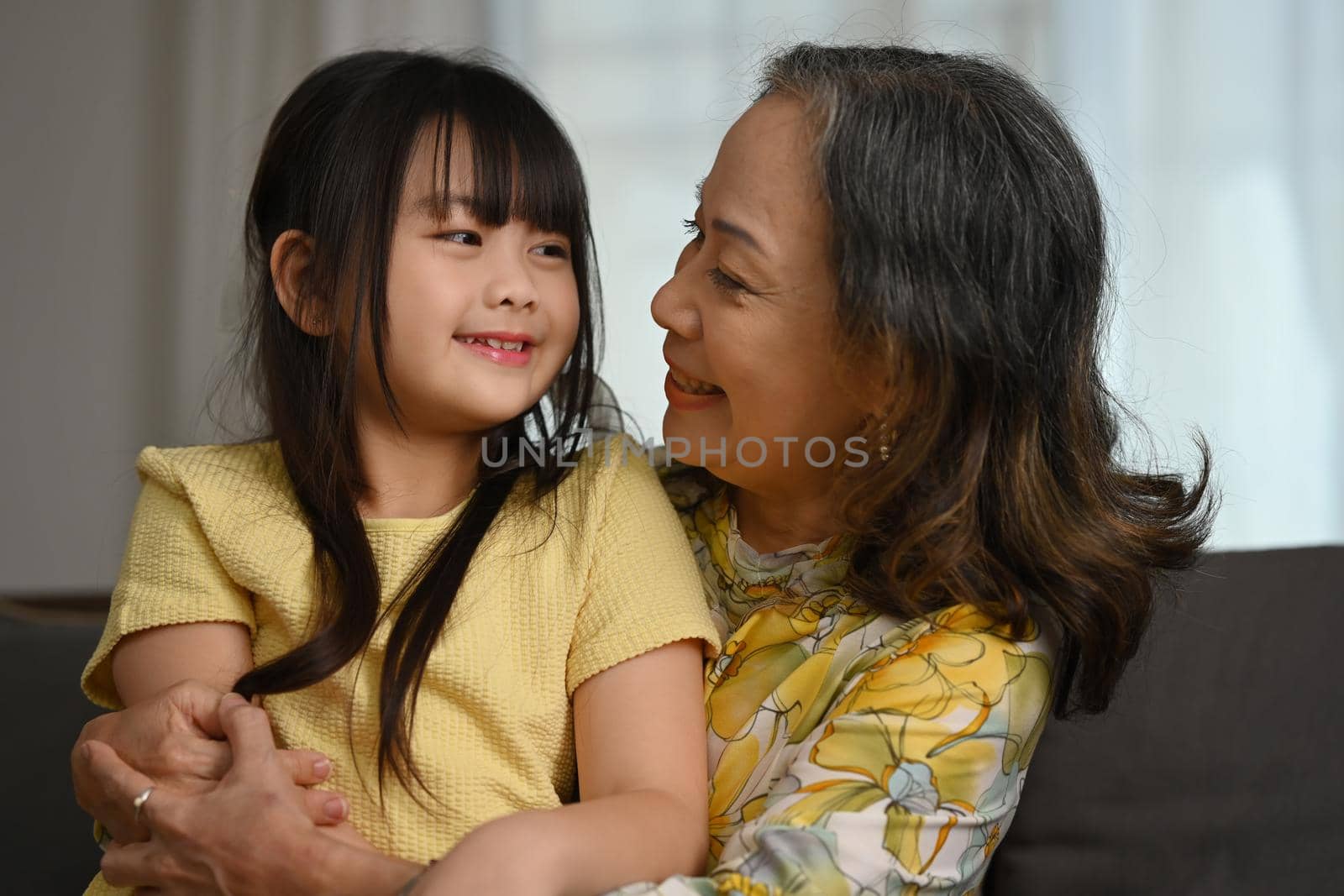 Affectionate grandmother hugging her adorable little grandchild, spending leisure weekend at home together. Loving family relationship concept.