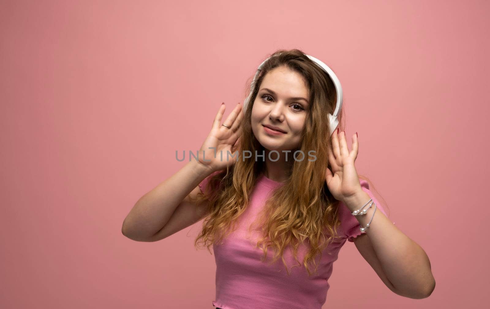 Young woman listening music in headphones with a smile face and stand over pink background. Attractive lady enjoying song copy space. People, music, emotions concept. by vovsht