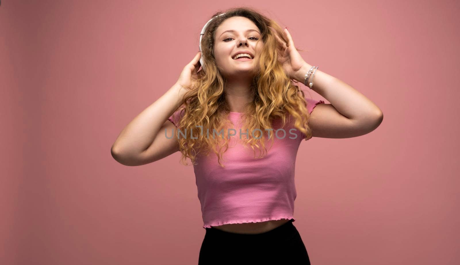 Young woman listening music in headphones and dancing with a smile face and stand over pink background. Attractive lady enjoying song copy space. by vovsht