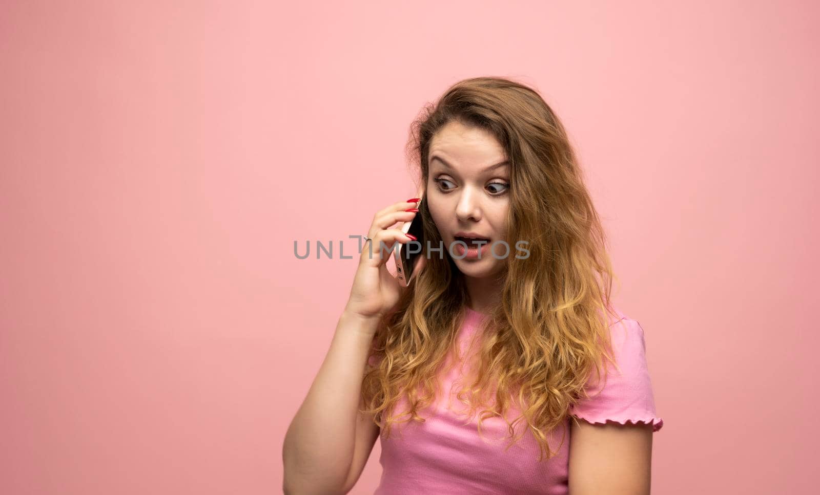 Happy surprised shocked young pretty woman speaking with a phone over pink wall background. Using mobile phone. by vovsht