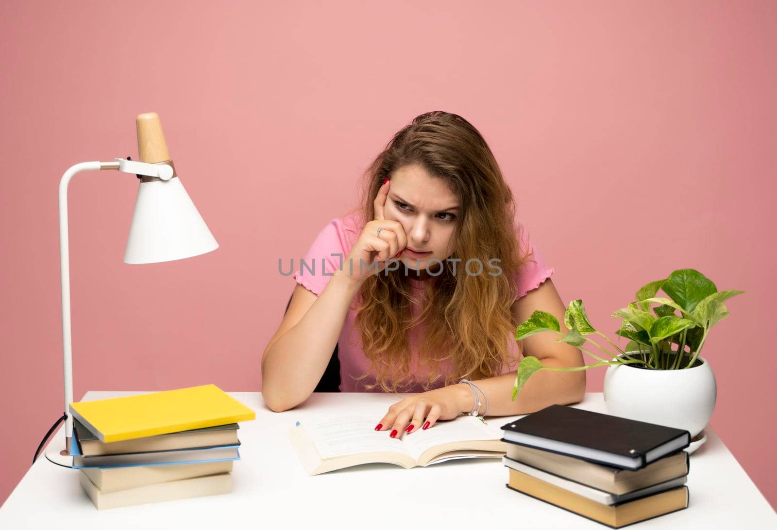 Young curly woman in a blue t-shirt studying from studio using laptop computer over a blue background. Serious beautiful young woman typing on laptop in a bright modern office