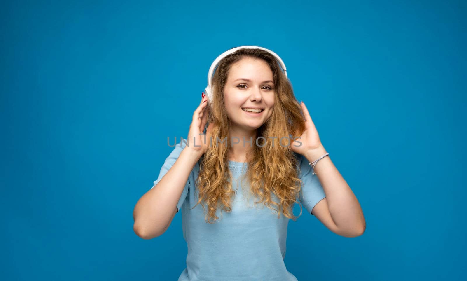 Energy girl with white headphones listening to music on blue background in studio