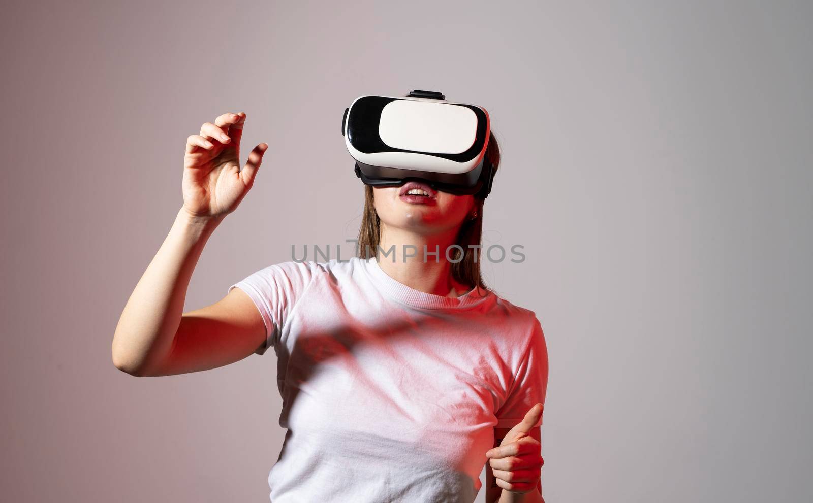 Young woman working in VR goggles on a grey background. Modern architect using virtual reality glasses at workplace. Designer working in augmented reality vr studio. by vovsht