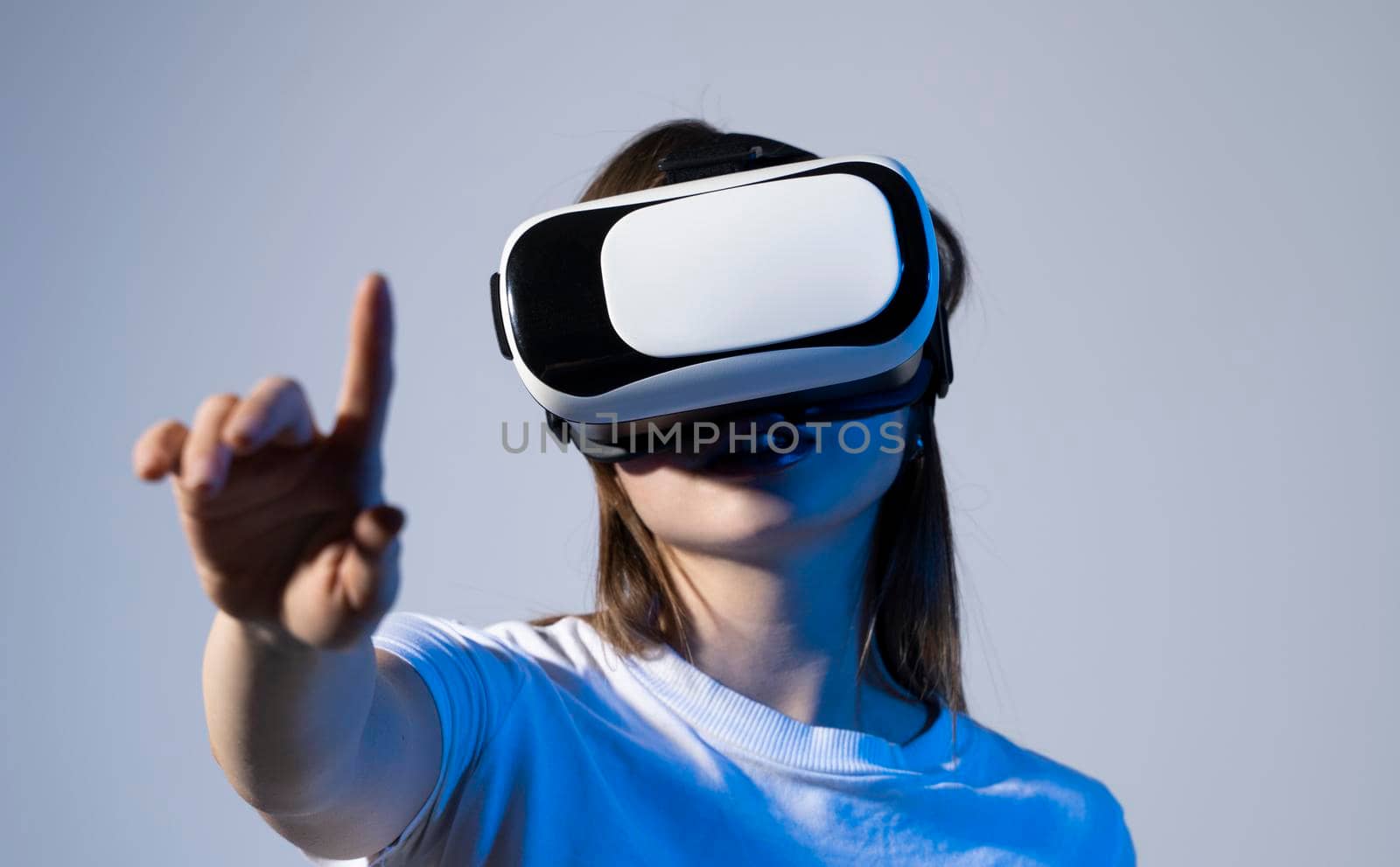 Close up of young woman stands in studio wearing VR glasses with a hand in air and trying to touch someting in virtual space. Virtual reality technology. by vovsht