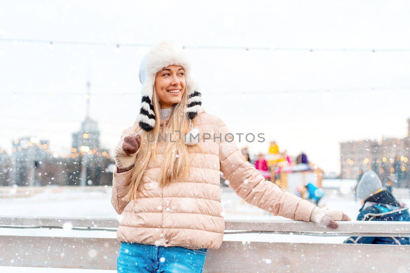 Medium shoot portrait of romantic european lady wears stylish winter jacket and funny fluffy hat in snowy day. Outdoor photo of inspired blonde woman enjoying free time in winter city. Christmas