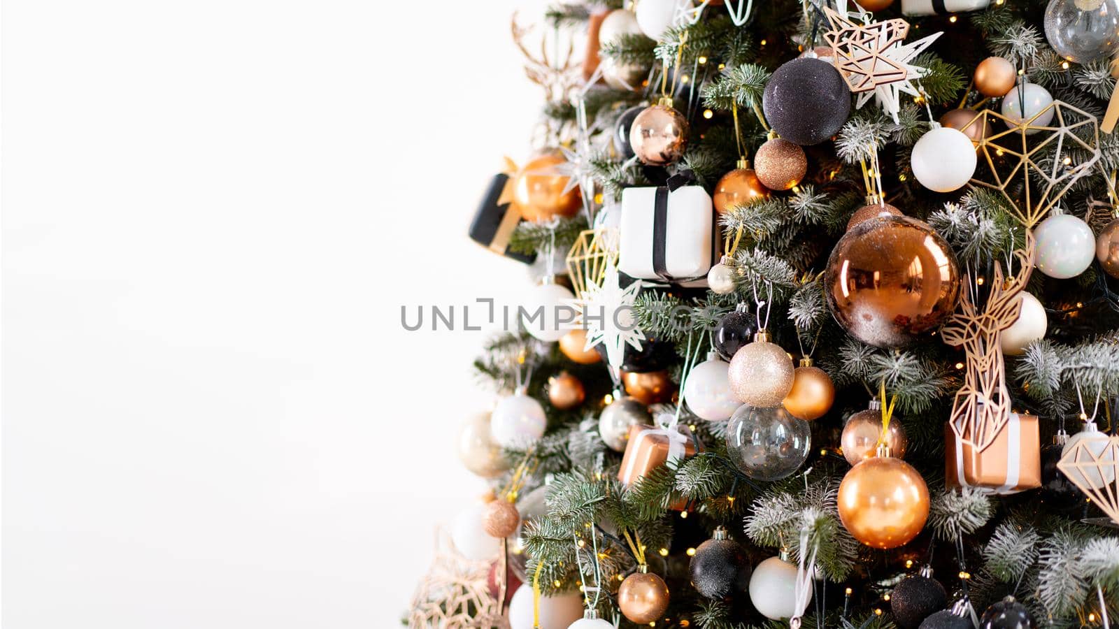 Christmas tree close up standing white wall background decorated white black gold color with light garland. Christmas decoration with copy space