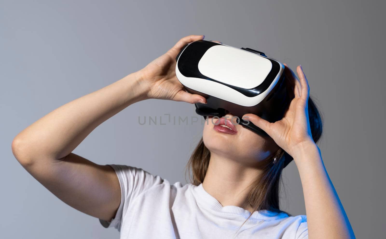 Young brunette woman wearing a virtual reality headset goggles and playing a game with a friends in metaverse. Future technology concept. by vovsht