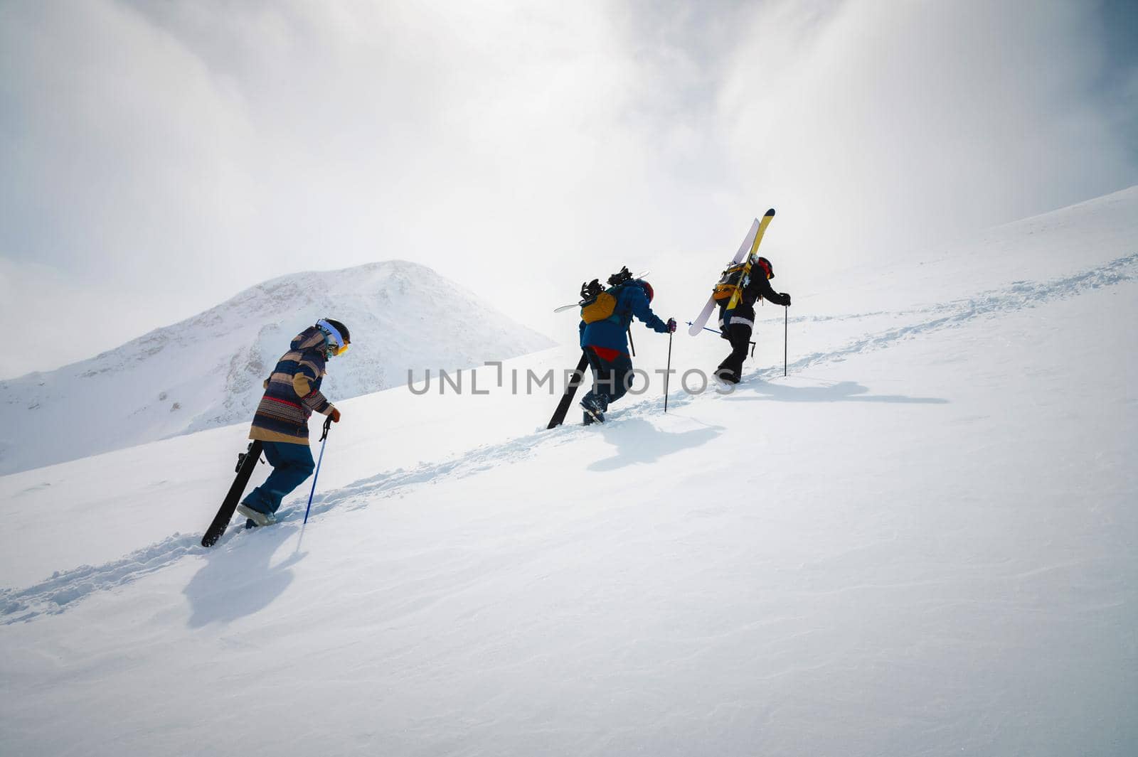 Three friends snowboarders skiers go uphill with a snowboard and skis in their hands for backcountry or freeride by yanik88