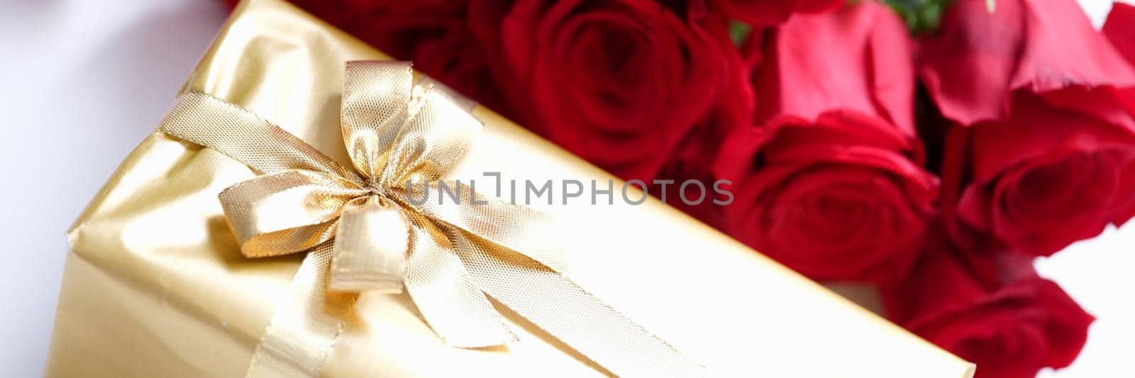Gift wrapped in gold and a bouquet of red roses, close-up. Beautiful fighting box with ribbon, floristry