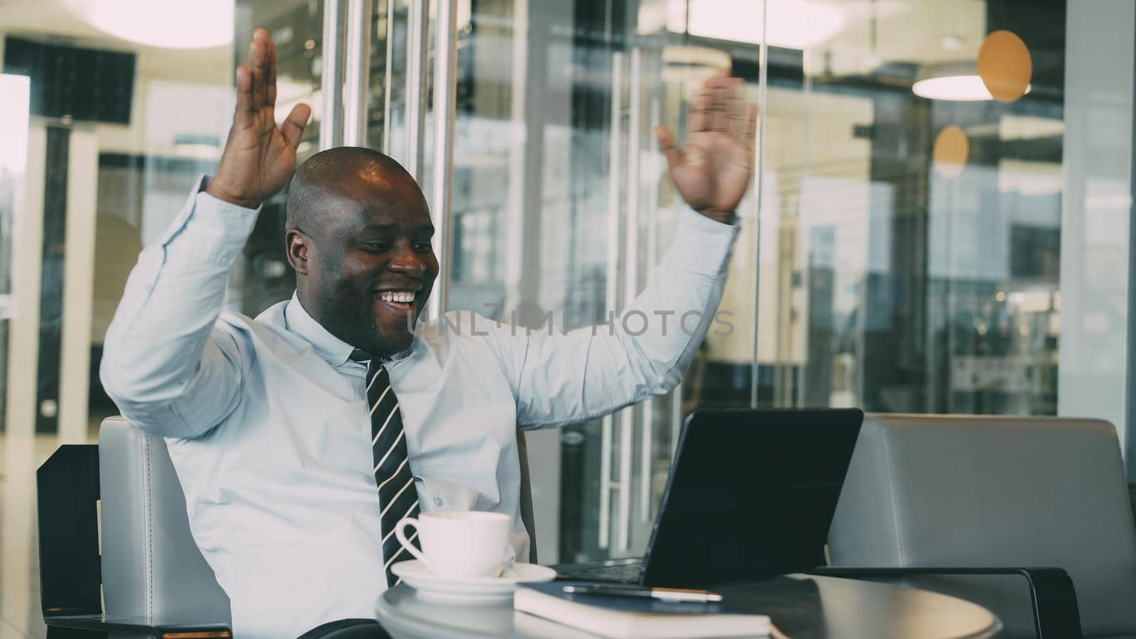 Successful african american businessman using laptop computer receiving good message and become very excited and dancing while sitting in modern cafe duiring coffee braek