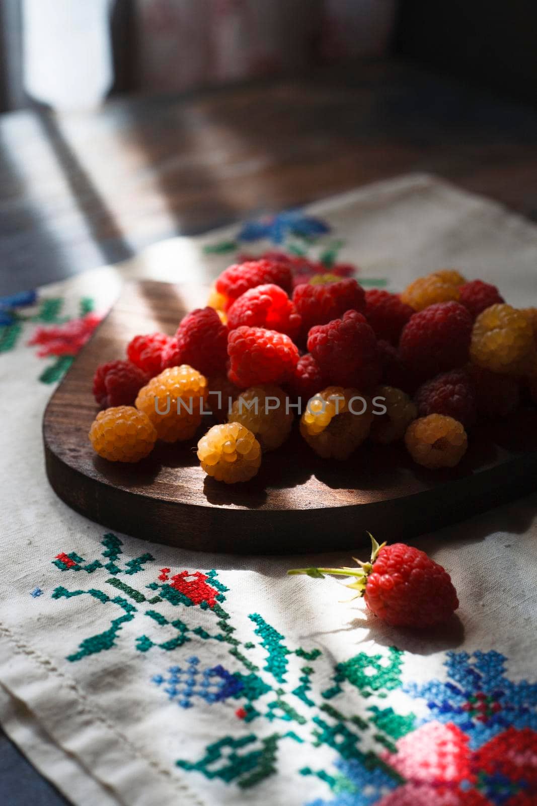 Red and yellow raspberry on wooden board on rustic embroidered towel, selective focus