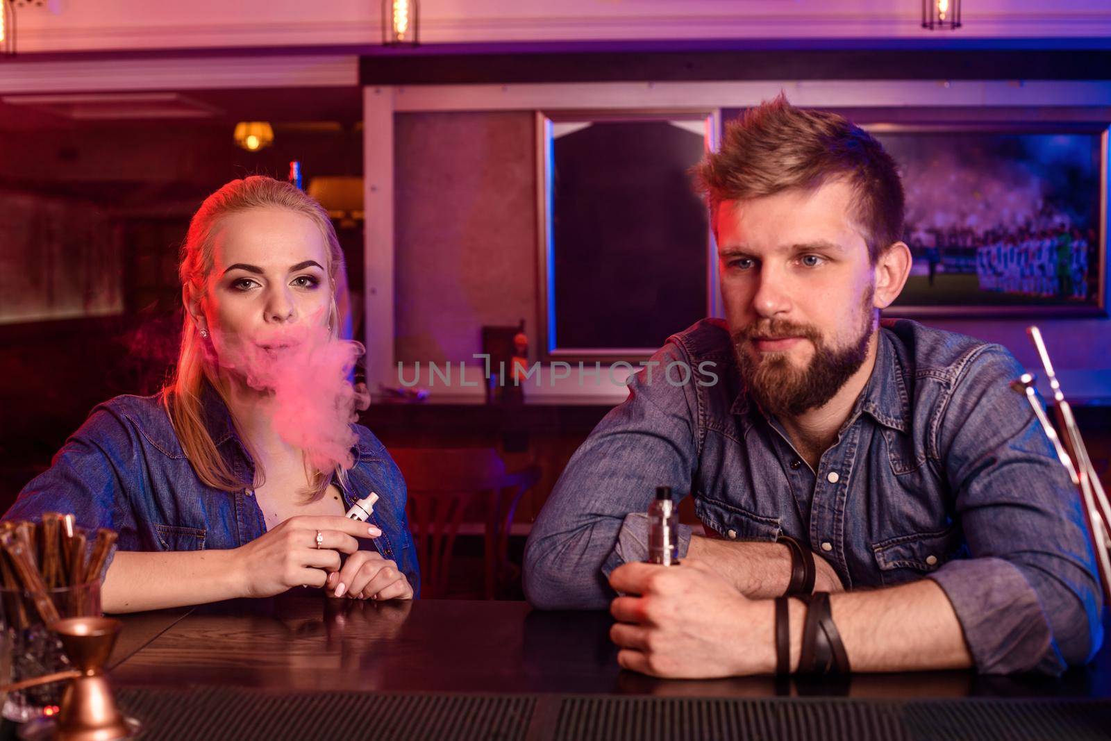 A man and woman smoking electronic cigarette in a vape bar. by nazarovsergey