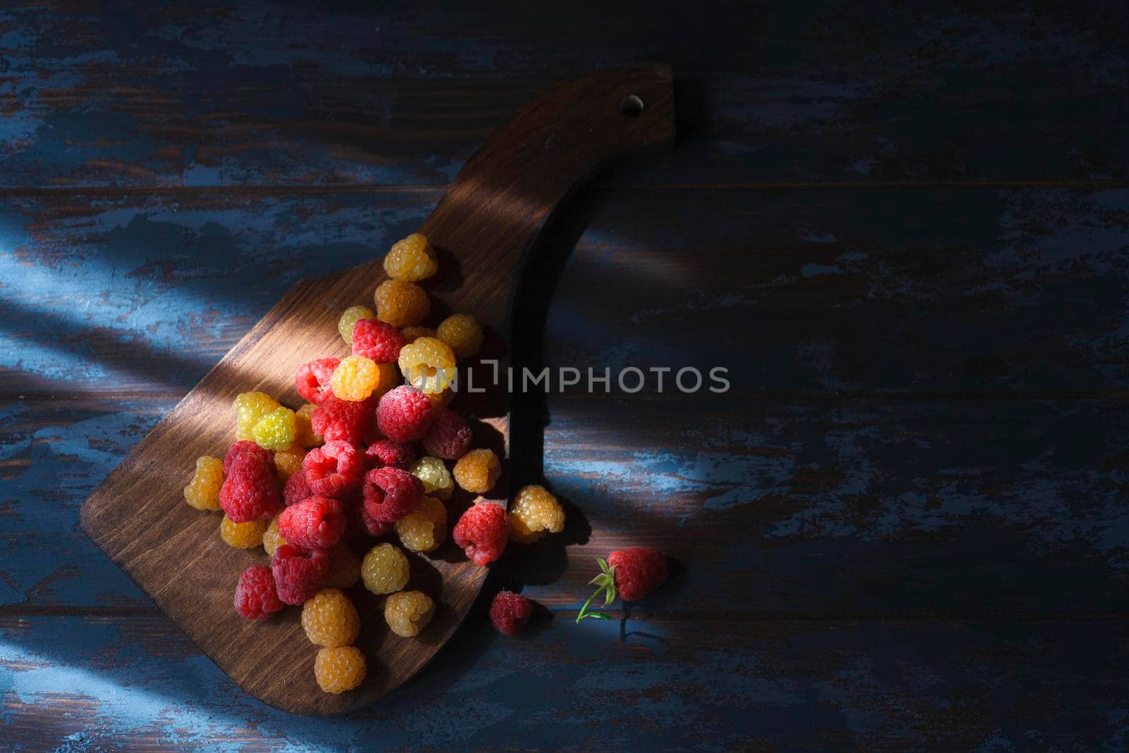 Red and yellow raspberry on wooden board, flatlay with copy space in low key