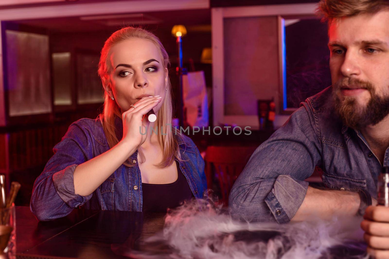 A man and woman smoking electronic cigarette in a vape bar. Vape shop