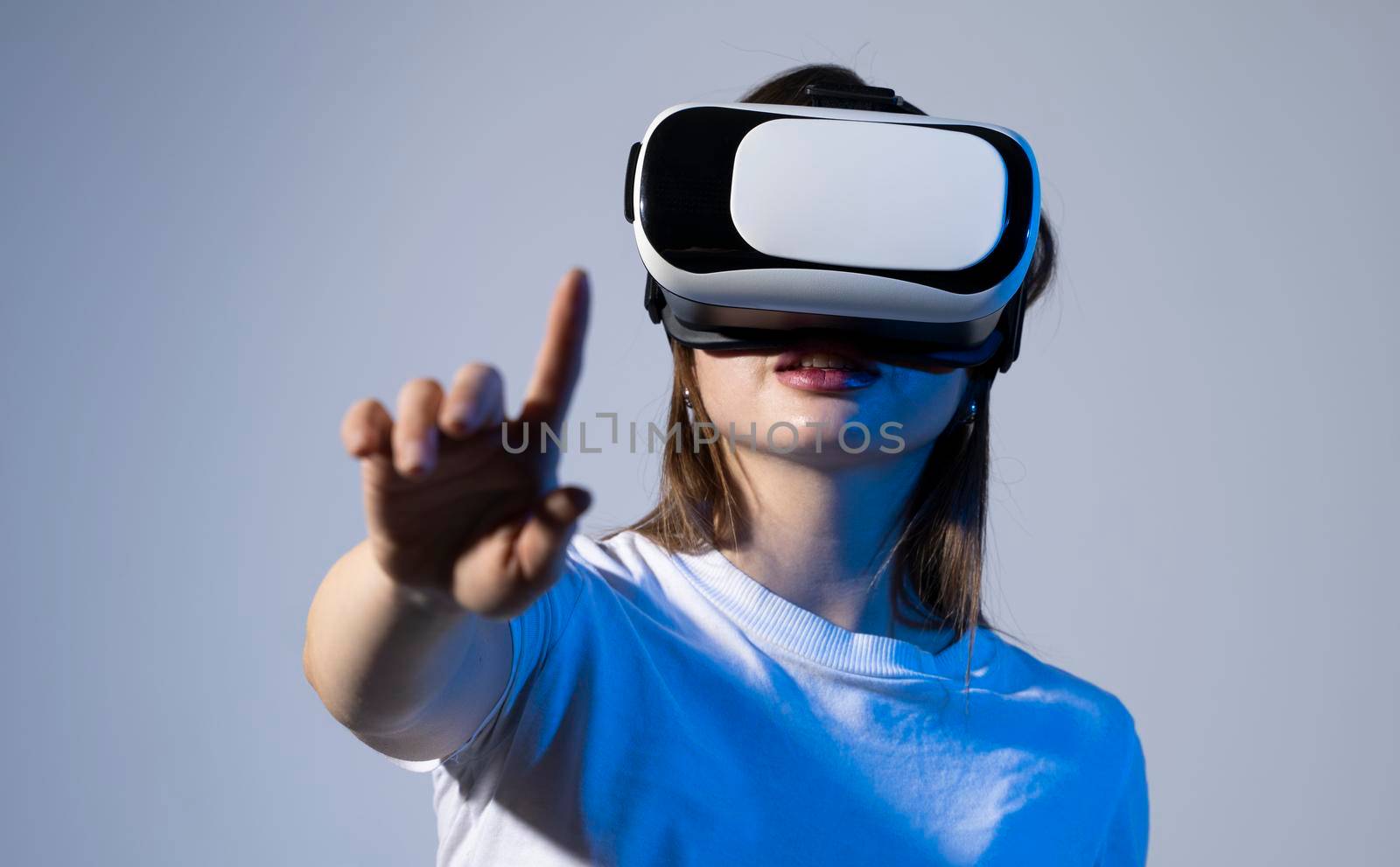 Young woman working in VR goggles on a grey background. Modern architect using virtual reality glasses at workplace. Designer working in augmented reality vr studio