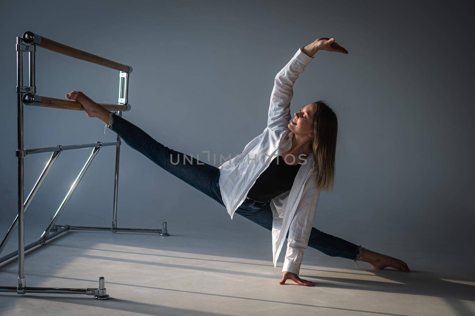 Caucasian woman in casual clothes pulls the split at the ballet barre