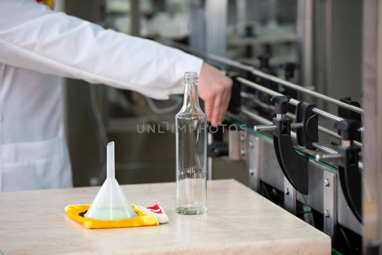 Worker hands and empty bottles on a conveyor belt in the production of alcoholic beverages.