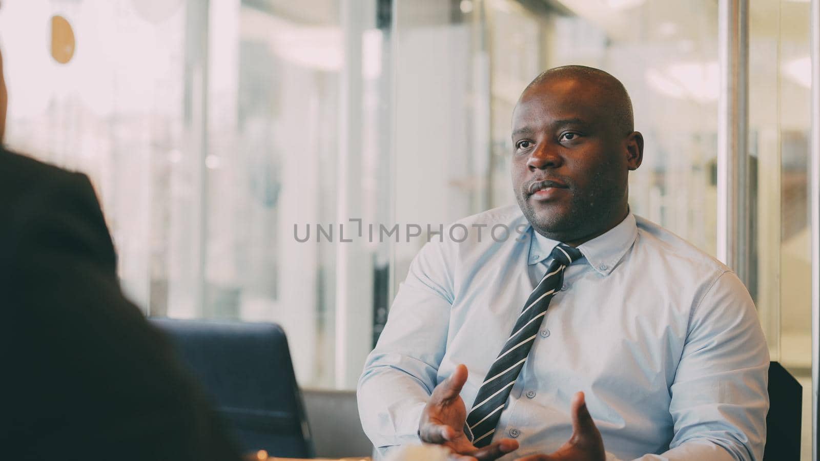 African American businessman gesticulating and explaining his startup details to investor in formal wear in glassy cafe during lunch time by silverkblack