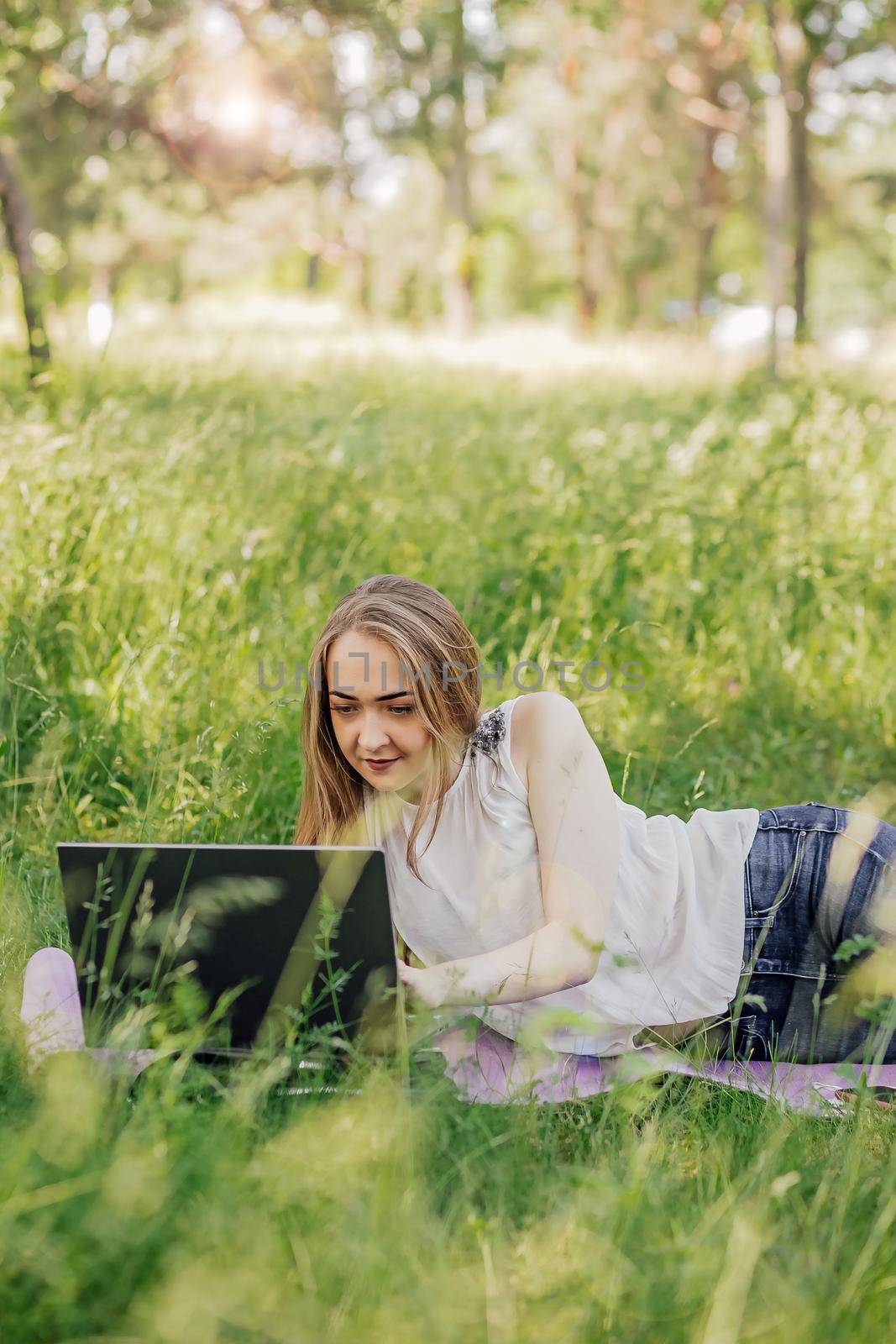 the girl sits on the grass and uses a laptop. Education, lifestyle, technology concept, outdoor learning concept by Anyatachka