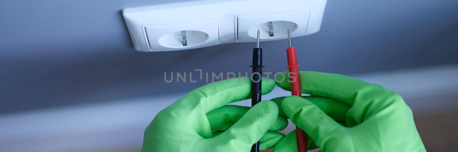 Gloved hands are holding a digital multimeter near the socket by kuprevich