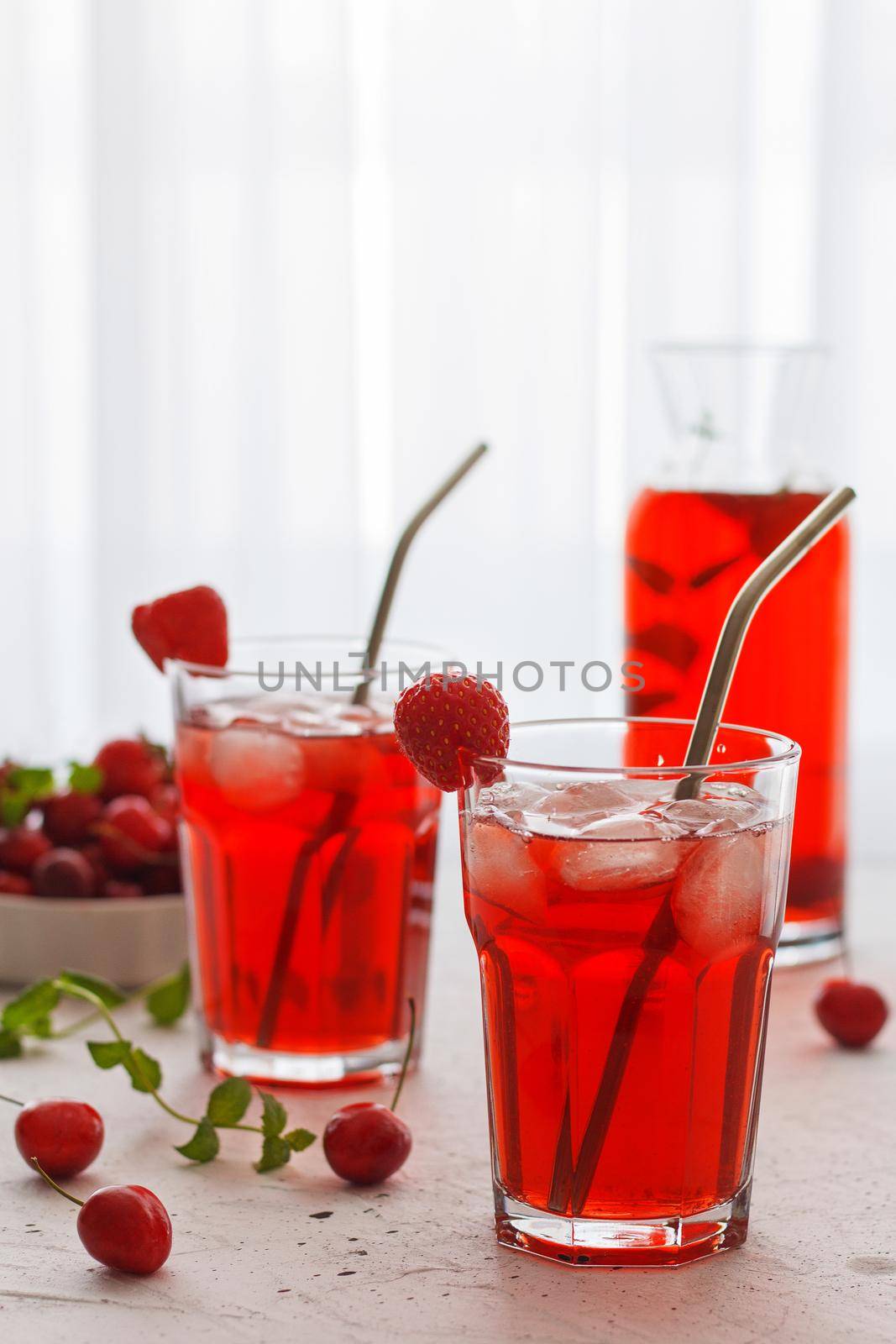 Red refreshing drink with mint on a gray background. Colorful summer non-alcoholic refreshing drink with ice made from berries. Vertical photo