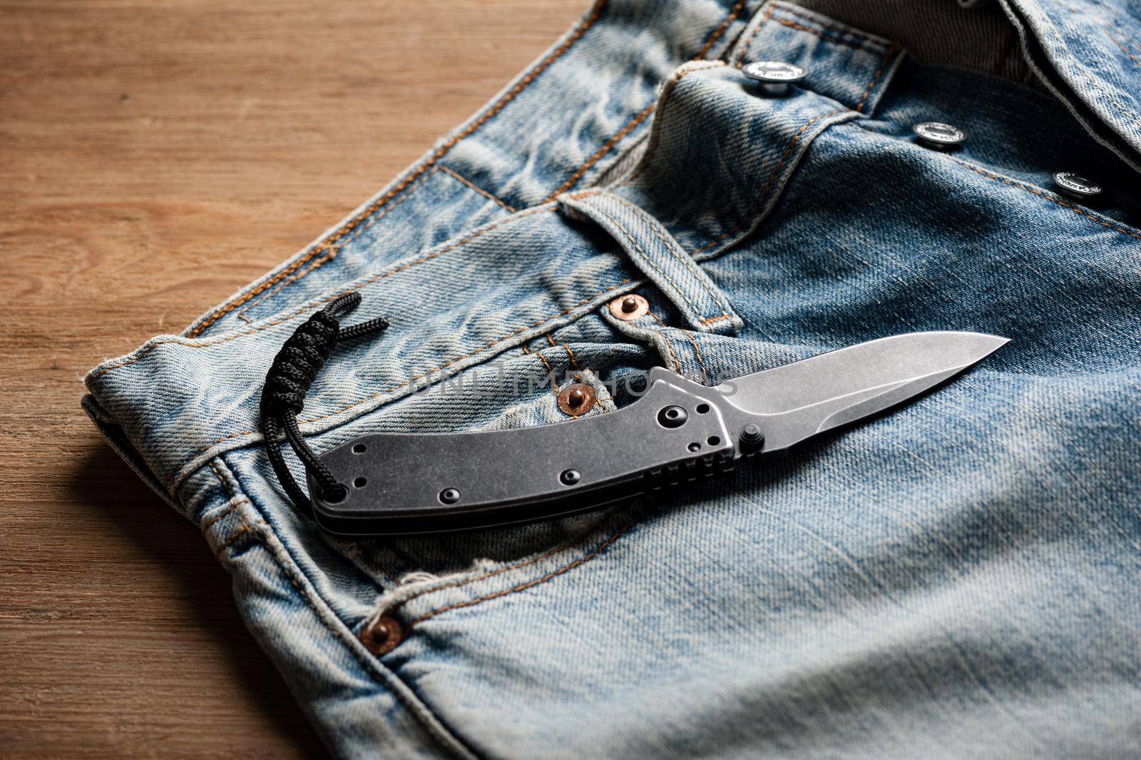 folding knife and jeans. closeup stainless steel pocketknife with blackwash finish on blade and handle.