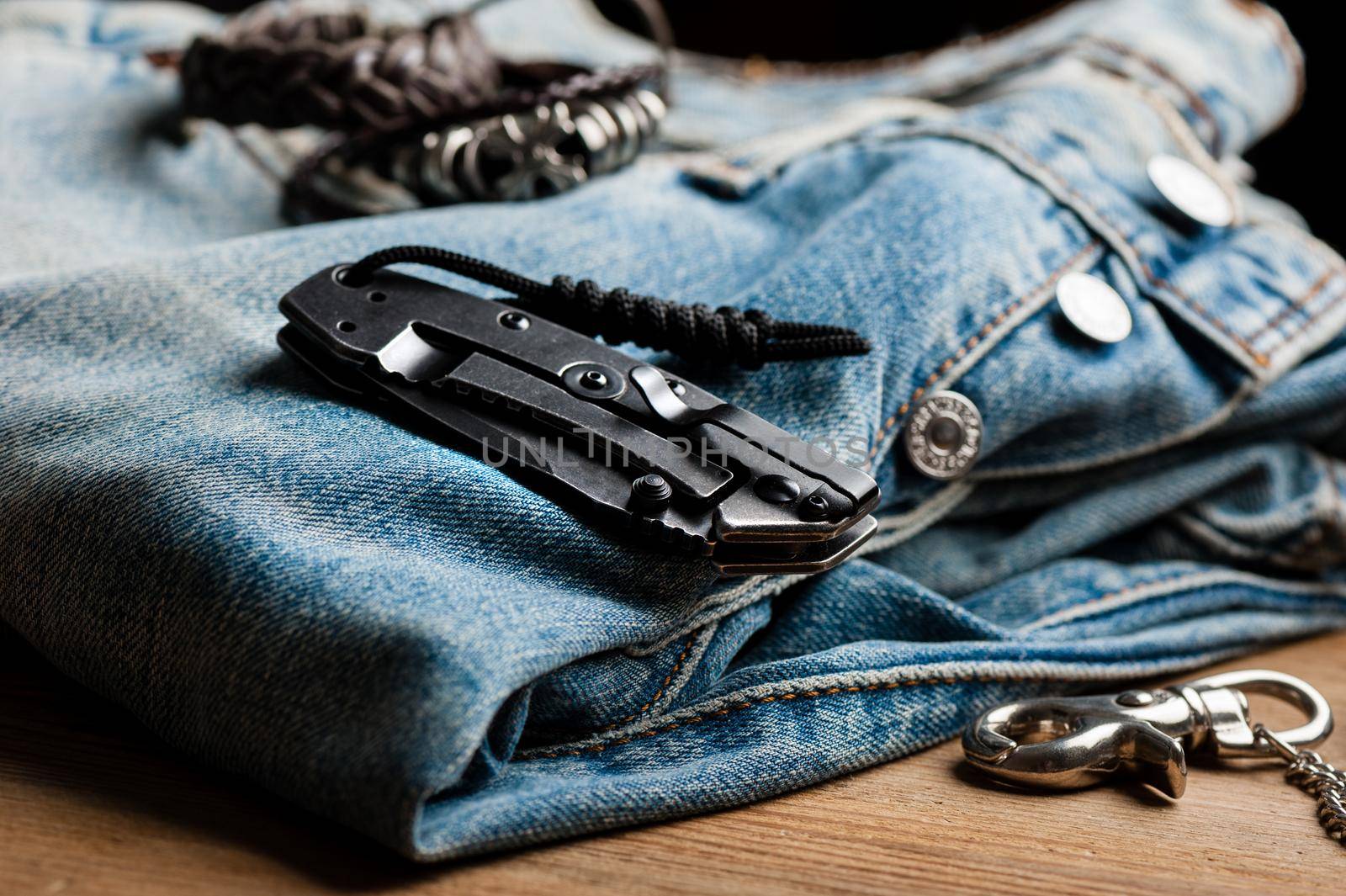 folding knife and jeans. closeup stainless steel pocketknife with blackwash finish on blade and handle.