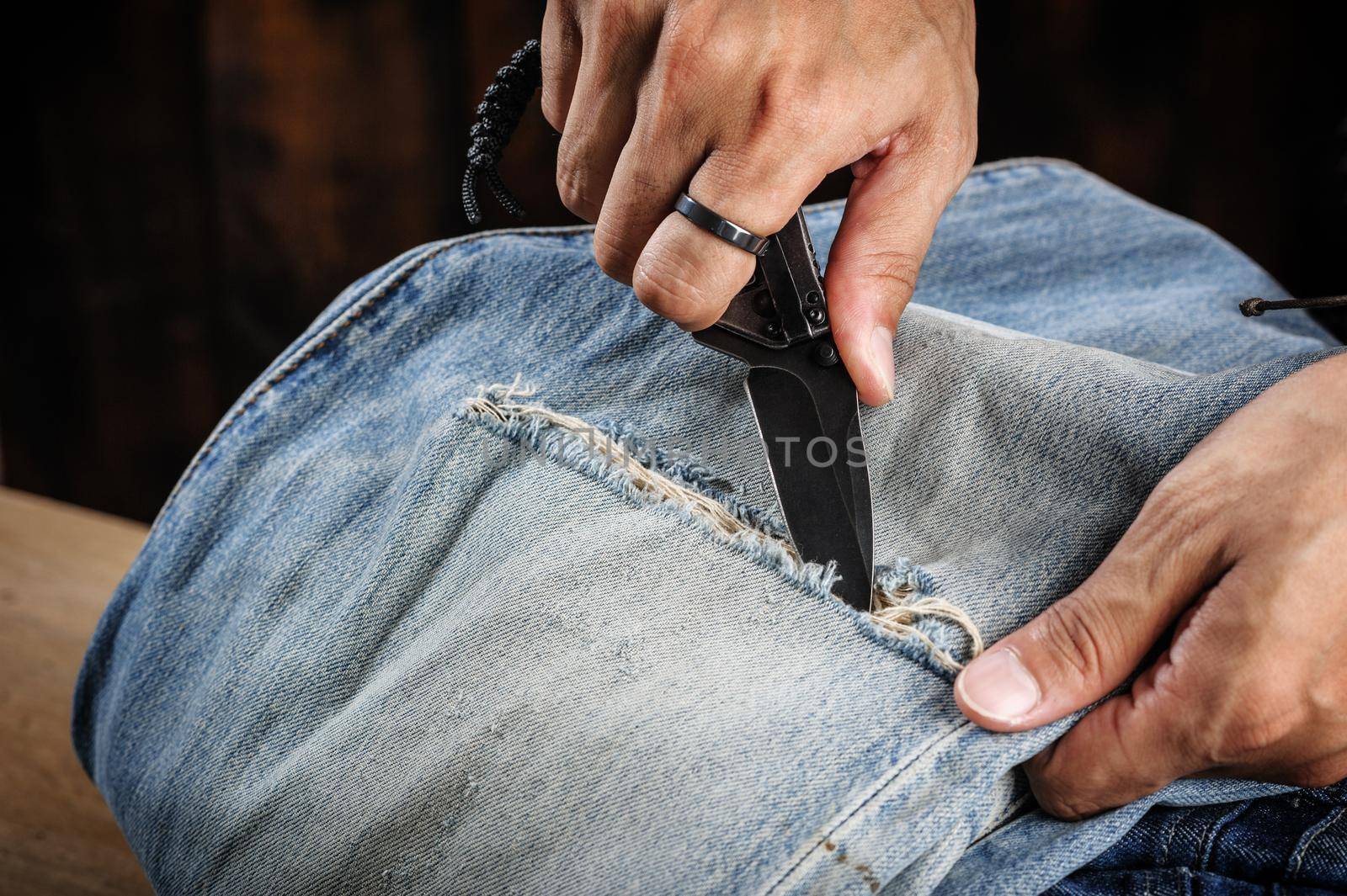 the man distressing jeans with folding knife.