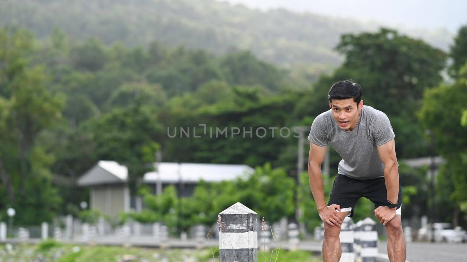 Tired young athletic man taking a break, resting after jogging in the park. Healthy lifestyle, workout and wellness concept.