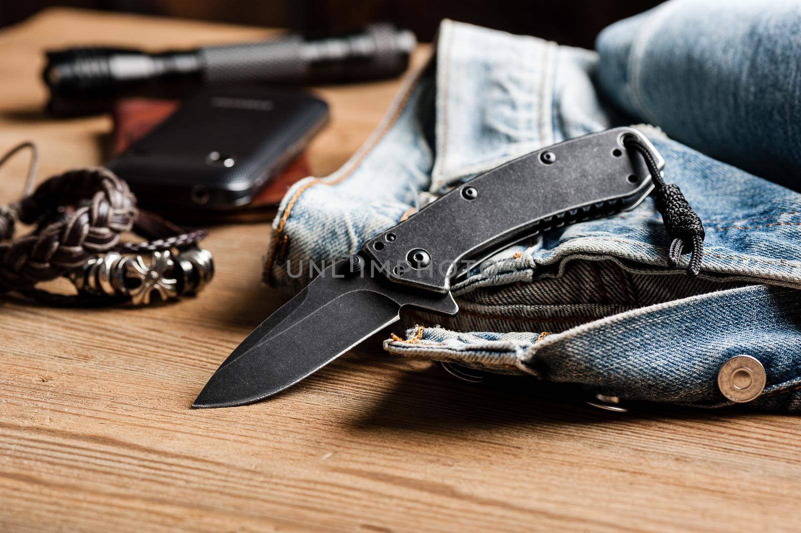 folding knife and jeans. closeup stainless steel pocketknife with blackwash finish on blade and handle.