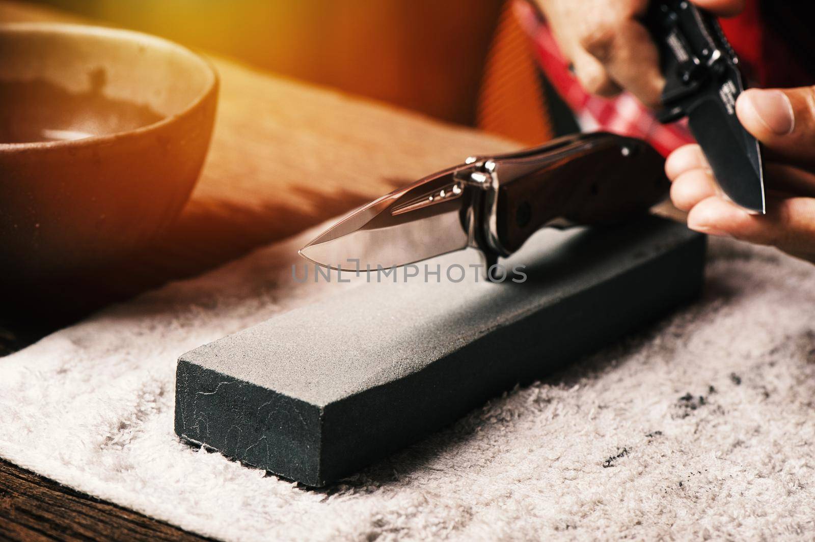 The man using whetstone to sharpening his pocket knife. Pocket knife care and maintenance concept.