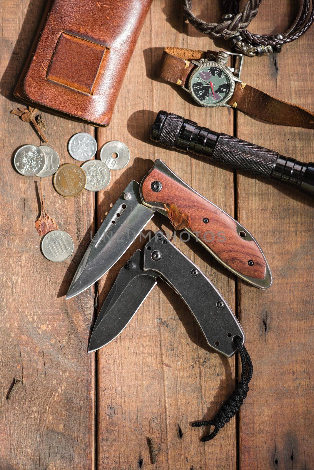 many men's items on wood plank, closeup at stainless steel folding knife.