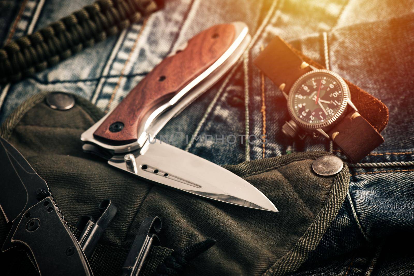 stainless steel folding knife and other everyday carry (EDC) items for men. closeup at folding knife. (low light and shallow depth of field)