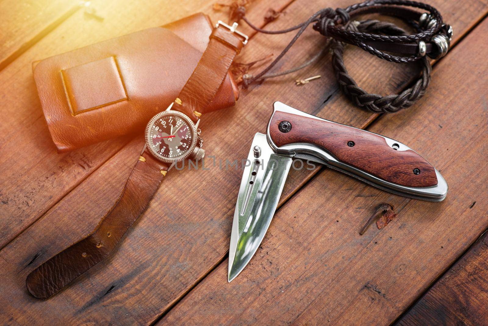 many men's items on wood plank, closeup at stainless steel folding knife.