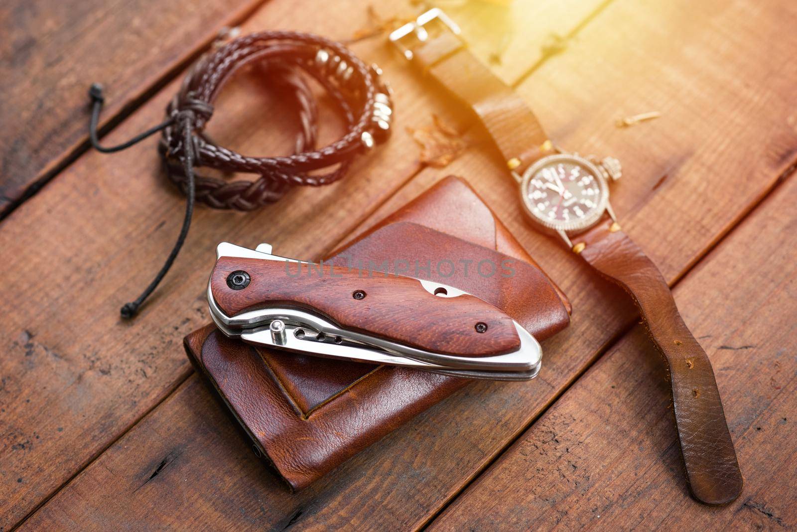 many men's items on wood plank, closeup at stainless steel folding knife.