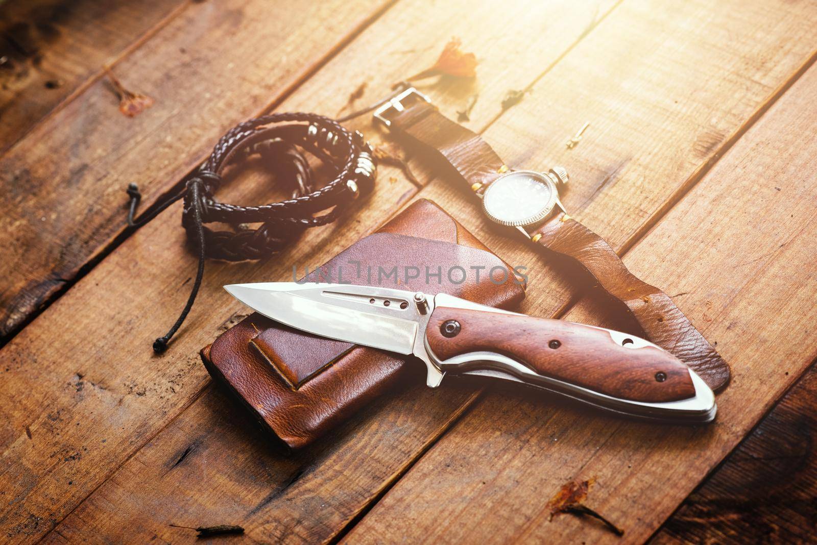 many men's items on wood plank, closeup at stainless steel folding knife.