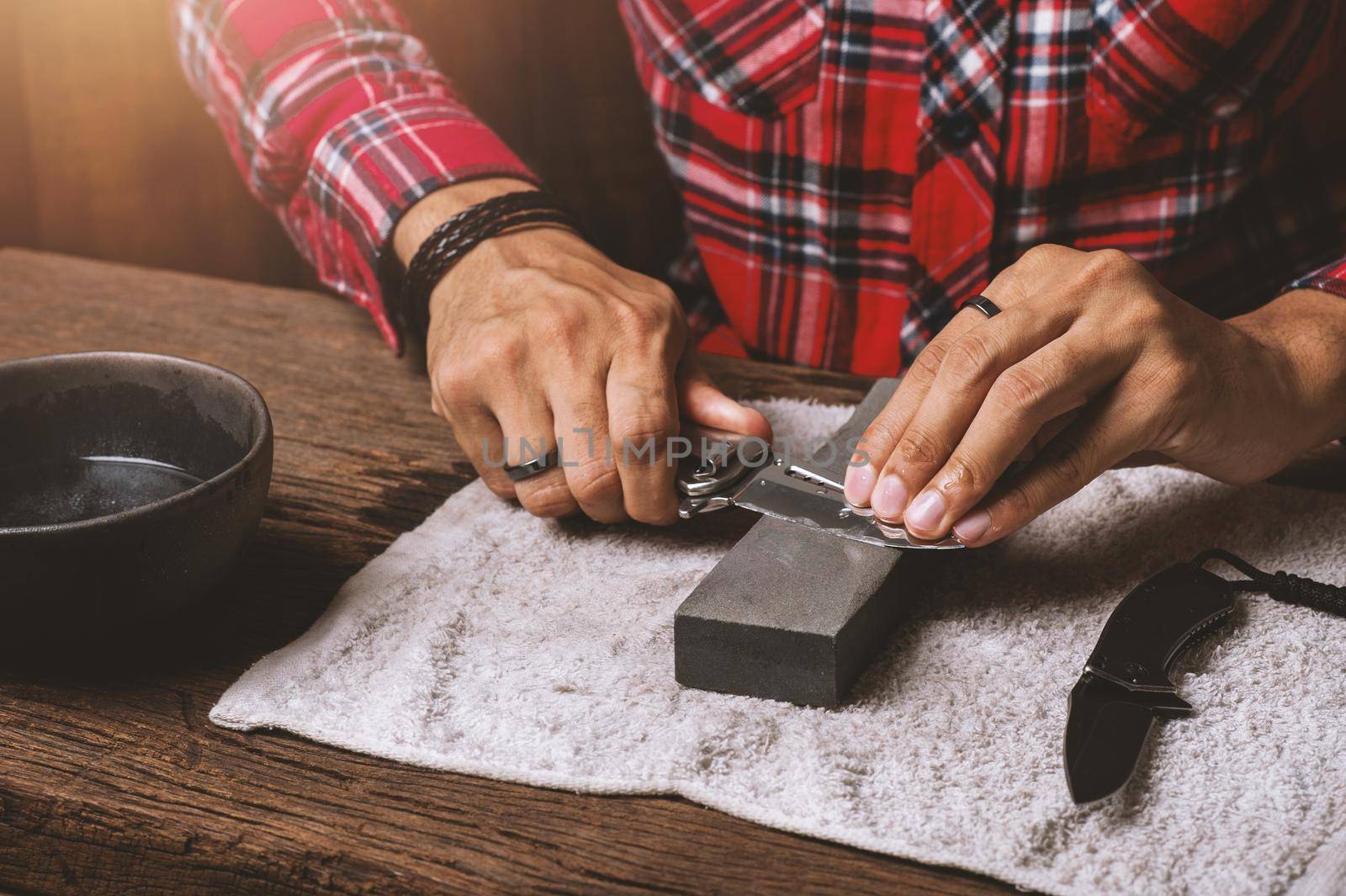 The man using whetstone to sharpening his pocket knife. Pocket knife care and maintenance concept.