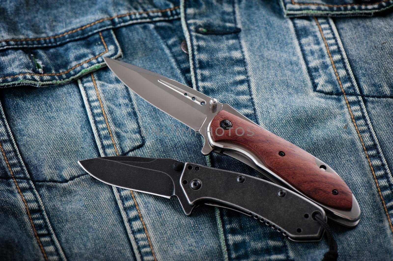 two stainless steel folding knifes over denim jacket