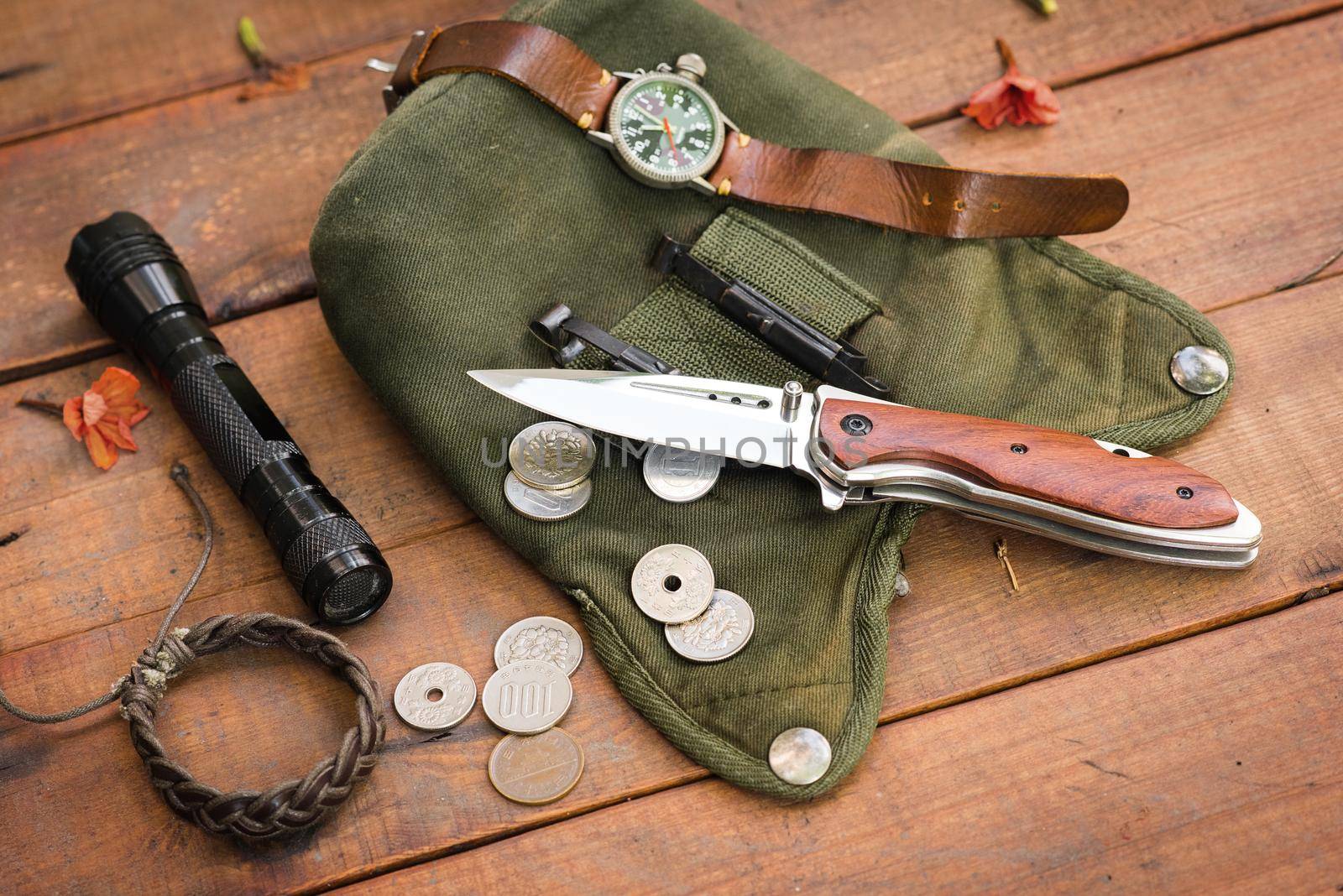 many men's items on wood plank, closeup at stainless steel folding knife.