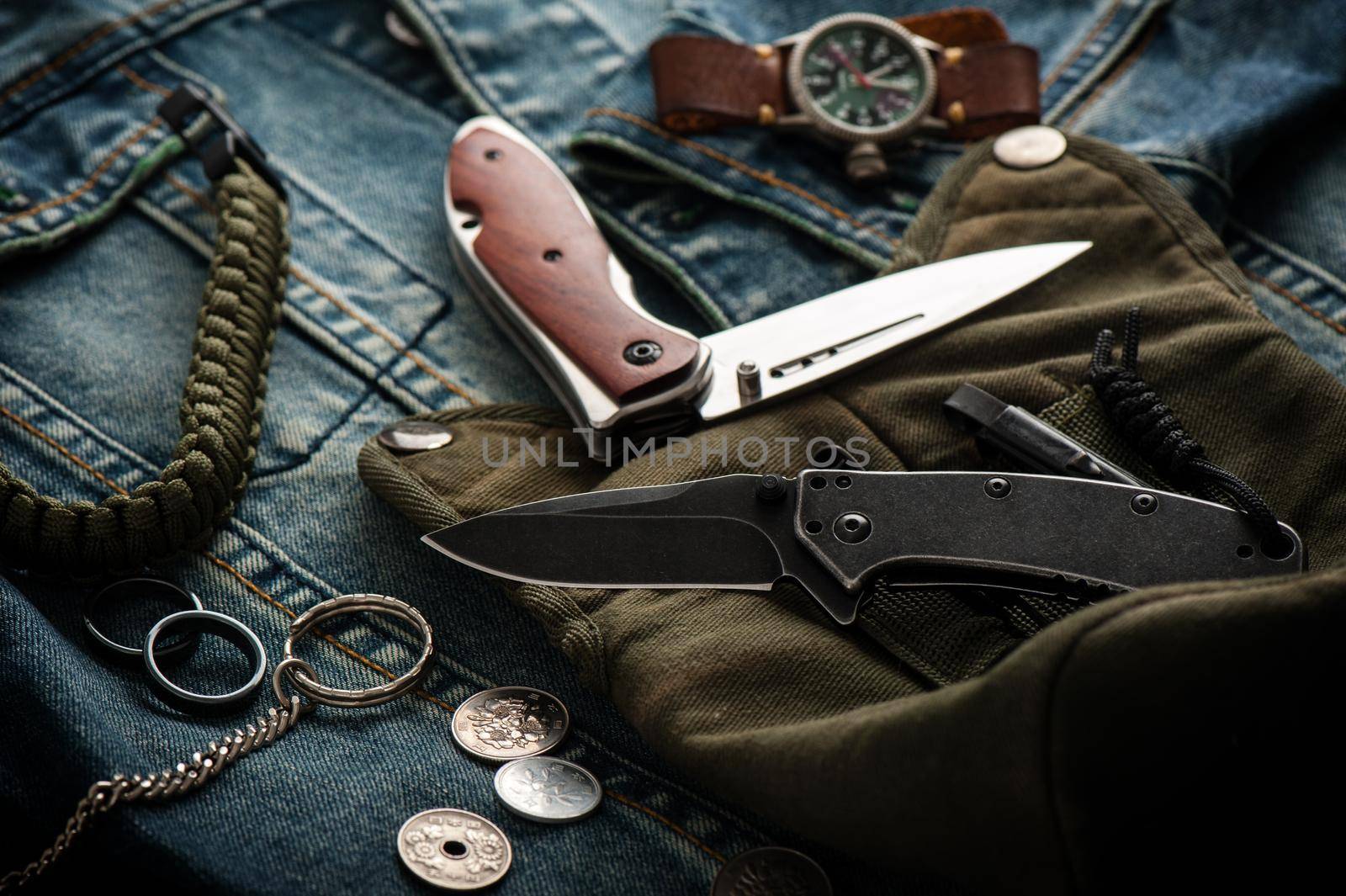 stainless steel folding knife and other everyday carry (EDC) items for men. closeup at folding knife. (low light and shallow depth of field)