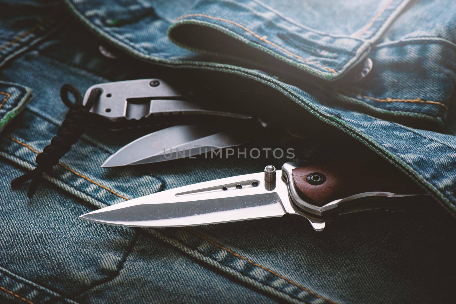 two stainless steel folding knifes over denim jacket